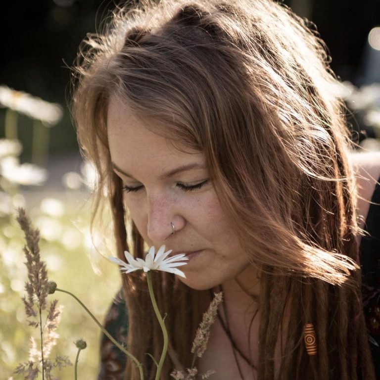 Frau mit langen Haaren beugt sich über eine Blume in einem Feld.