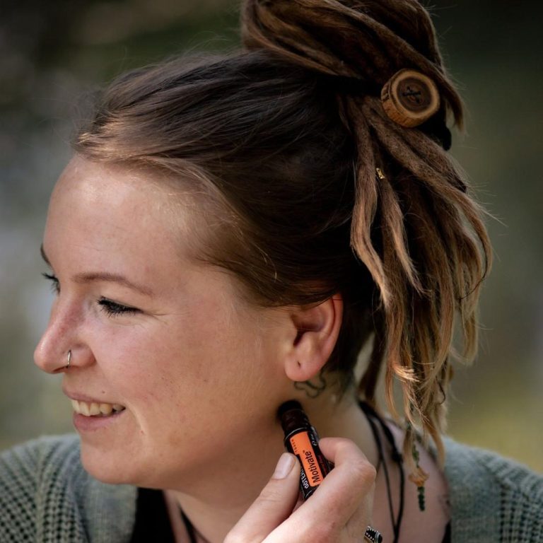 Junge Frau mit Dreadlocks, die lächelnd ein Produkt auf ihre Haut aufträgt.